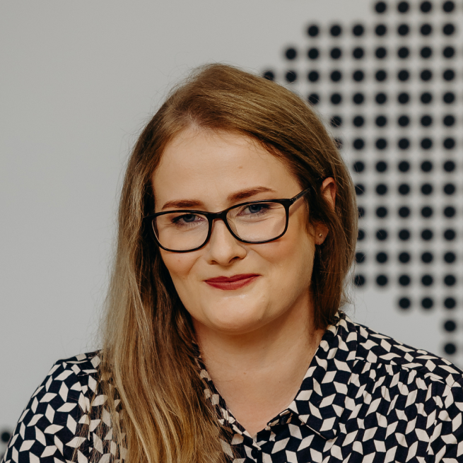 A woman wearing glasses and a black and white shirt, smiling confidently in a casual setting
