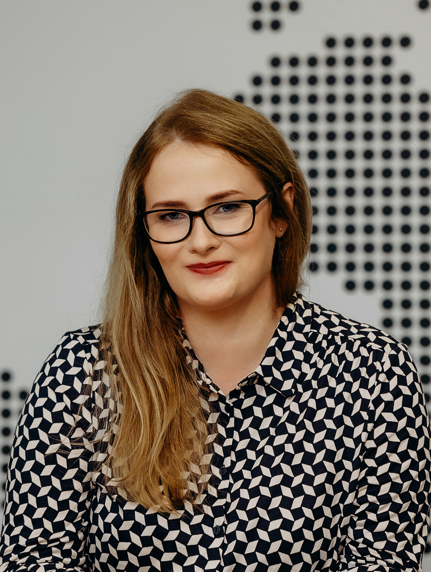 A woman wearing glasses and a black and white shirt, smiling confidently in a casual setting