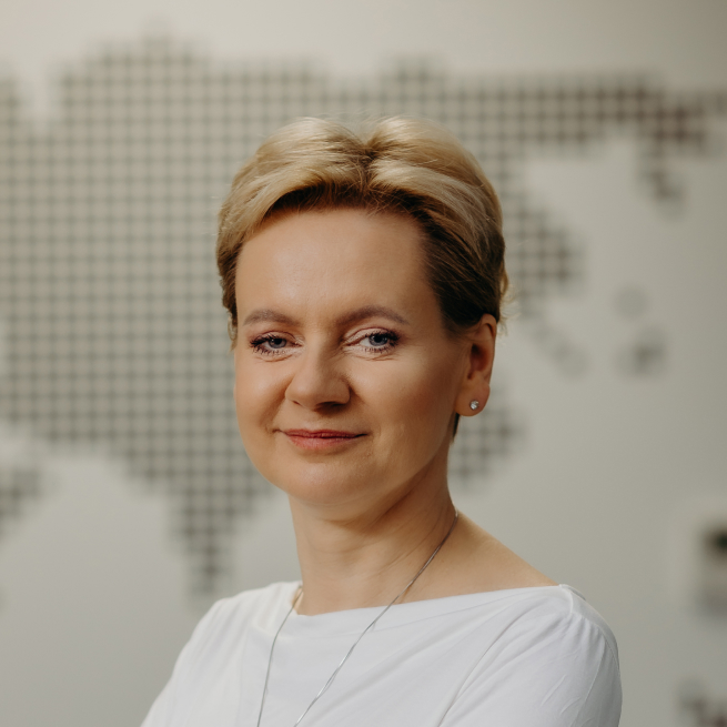 A woman with short blonde hair stands confidently in front of a map,