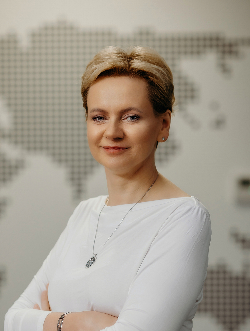 A woman with short blonde hair stands confidently in front of a map,