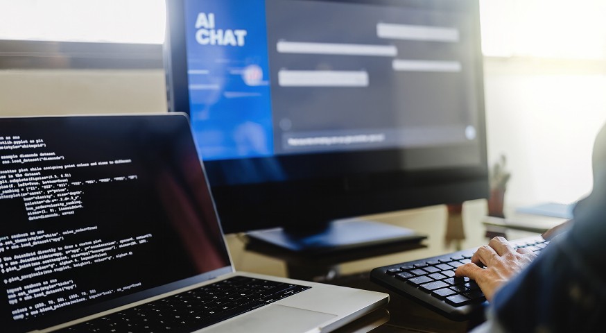 Developer coding on a laptop while referencing an AI Chat interface on a larger external monitor.
