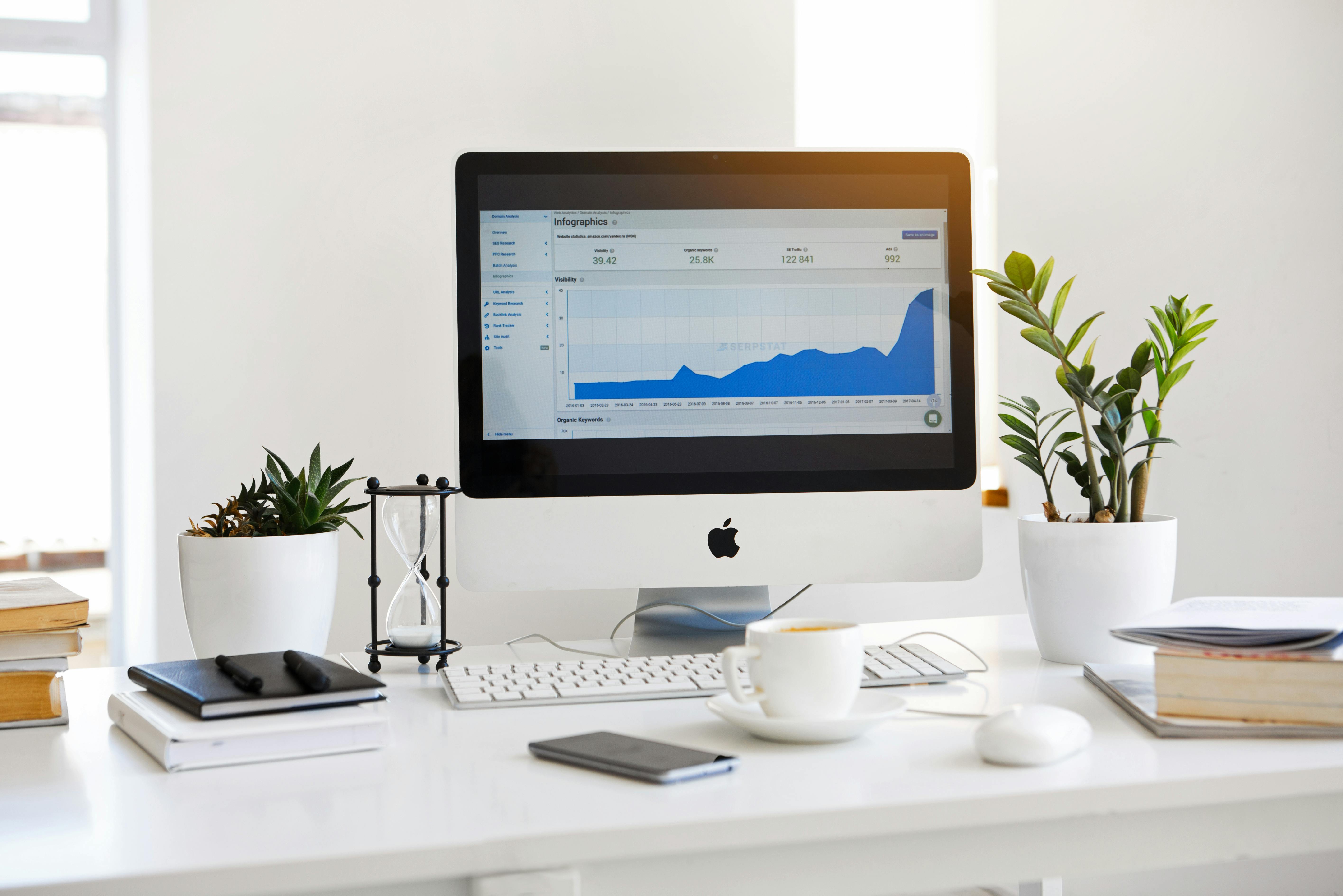 Computer on a desk displaying a graph, surrounded by plants and office supplies.
