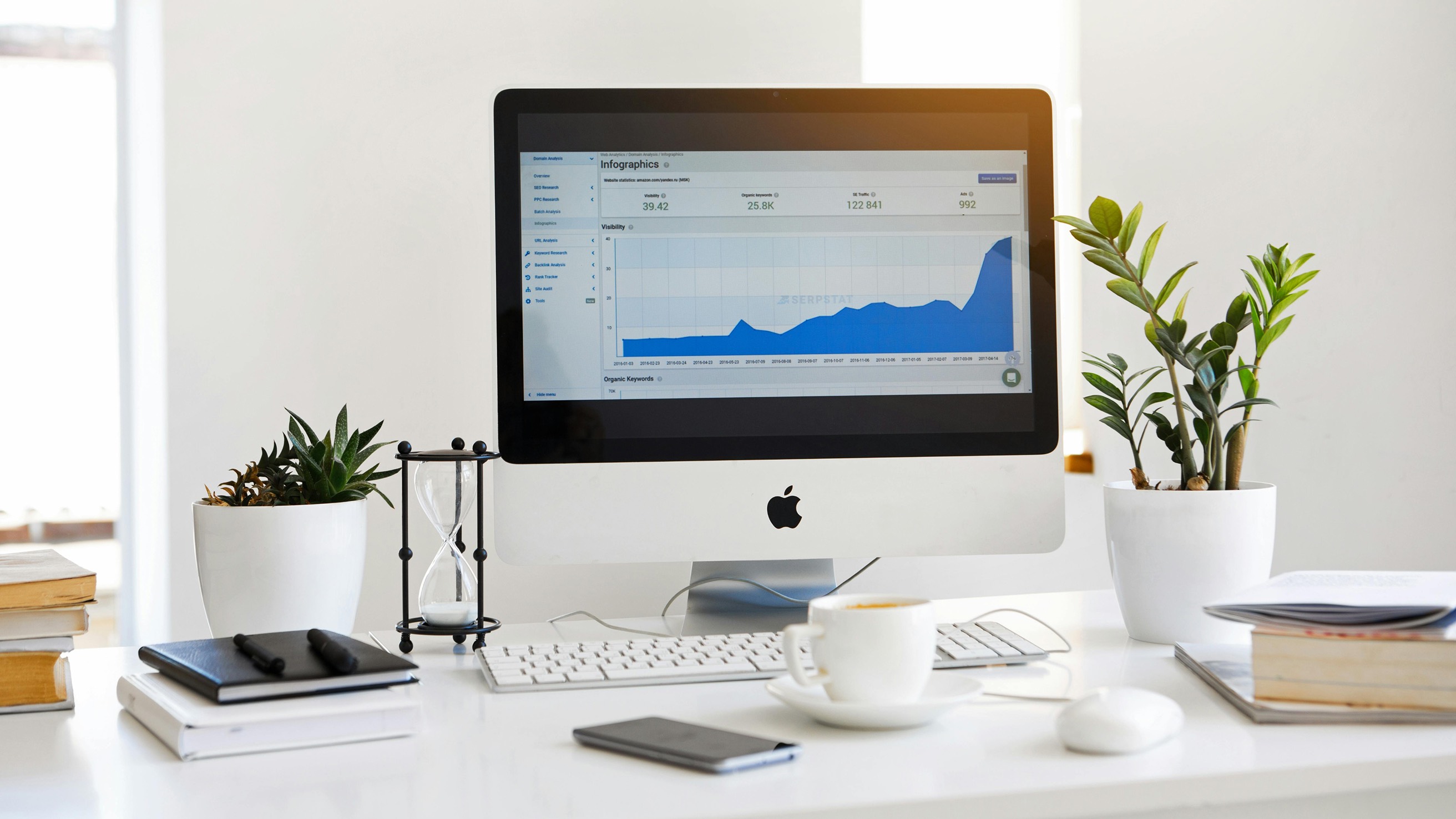 Computer on a desk displaying a graph, surrounded by plants and office supplies.
