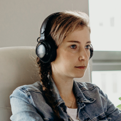A woman looking at the monitor with headphones on.