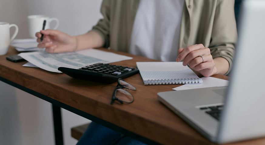 Person at desk working with calculator, laptop, and financial papers