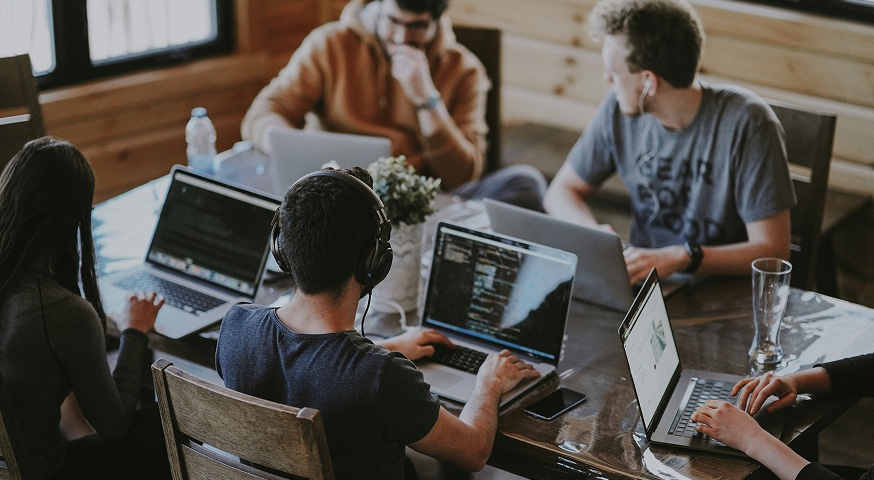 Software developers collaborating at shared workspace with laptops