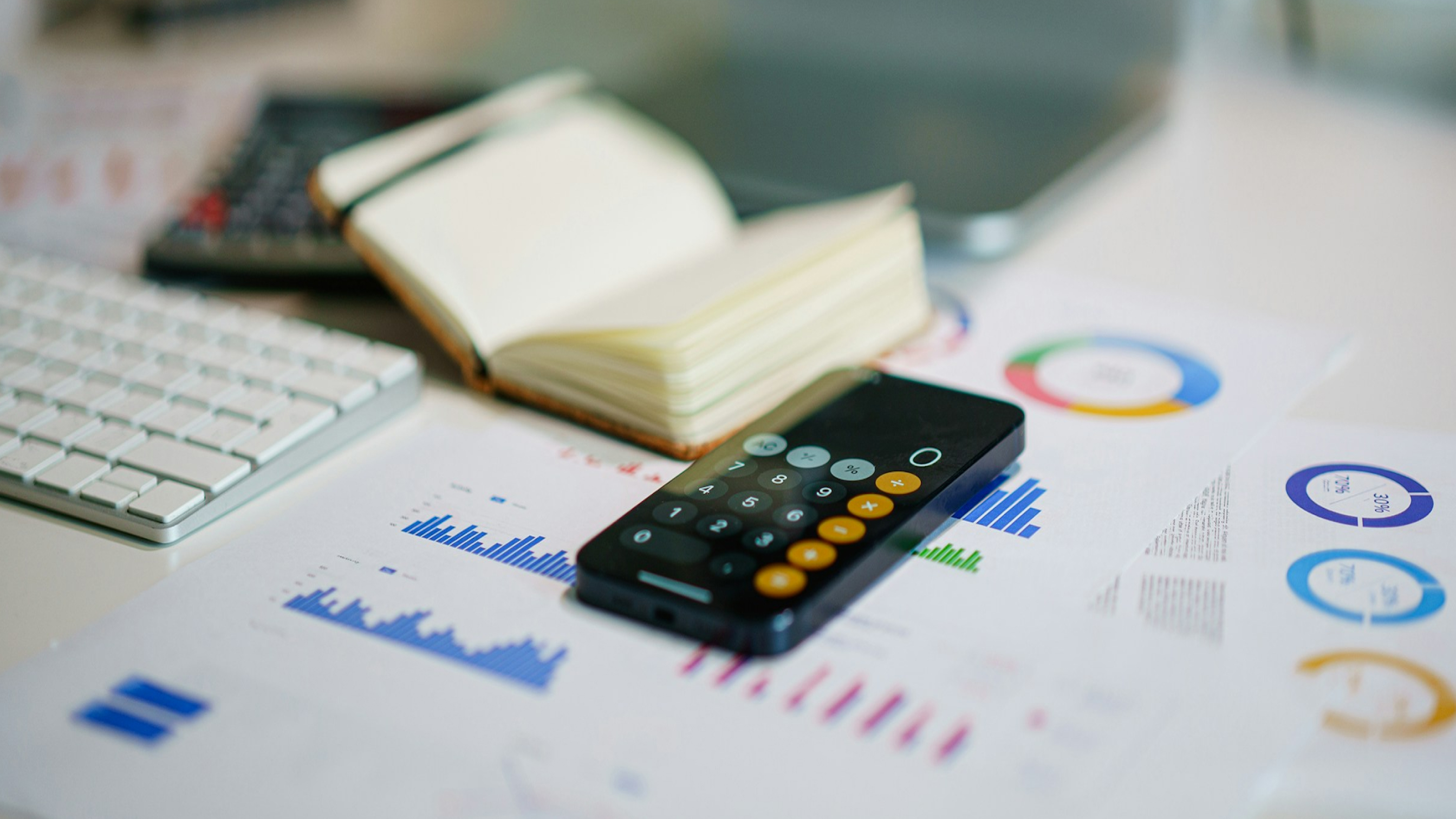 A smartphone lying on documents with graphs, next to a notebook and keyboard, representing financial data and personal loans.