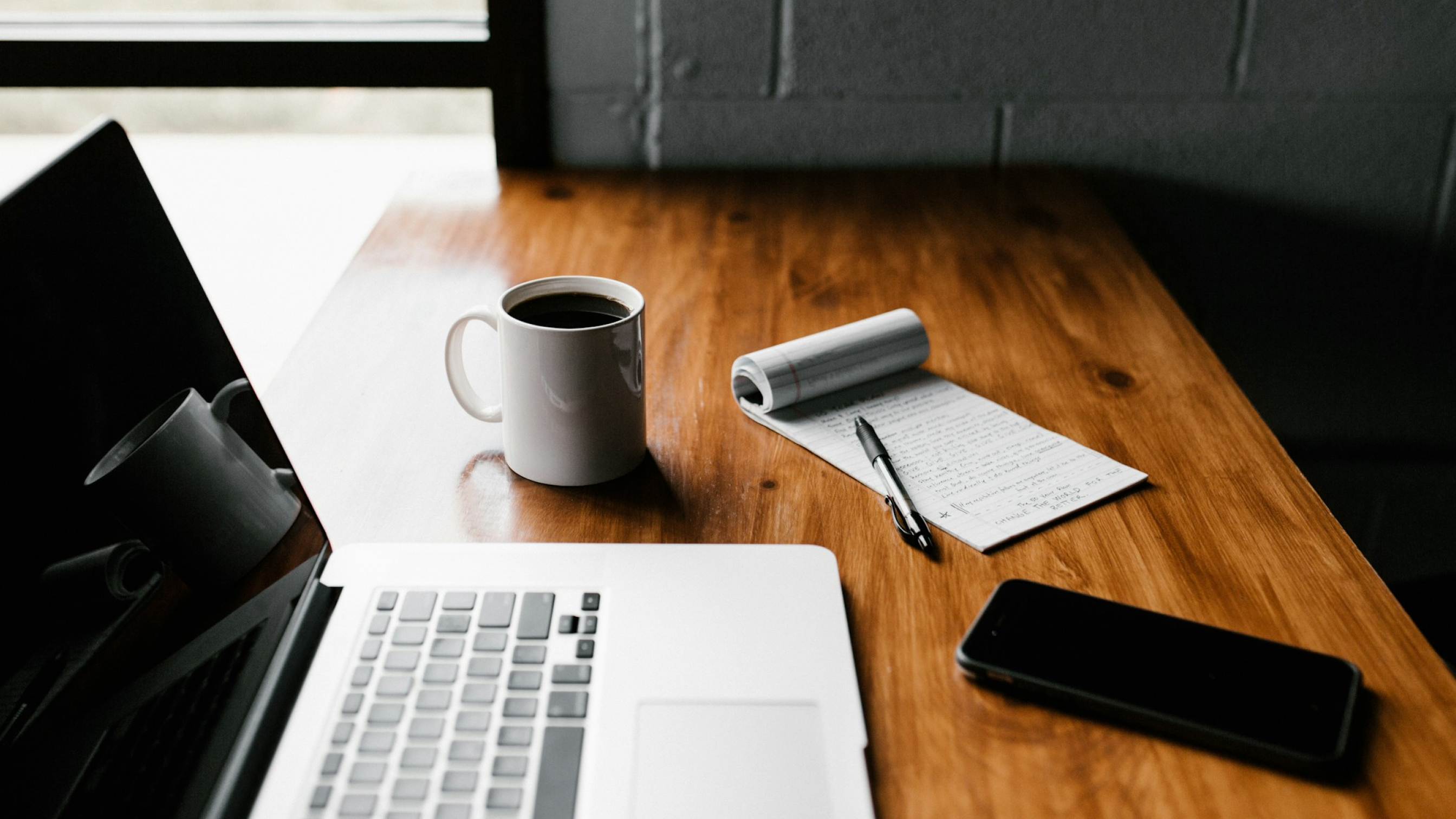 A coffee cup next to a laptop and notebook on a desk, representing automated workflow processes.