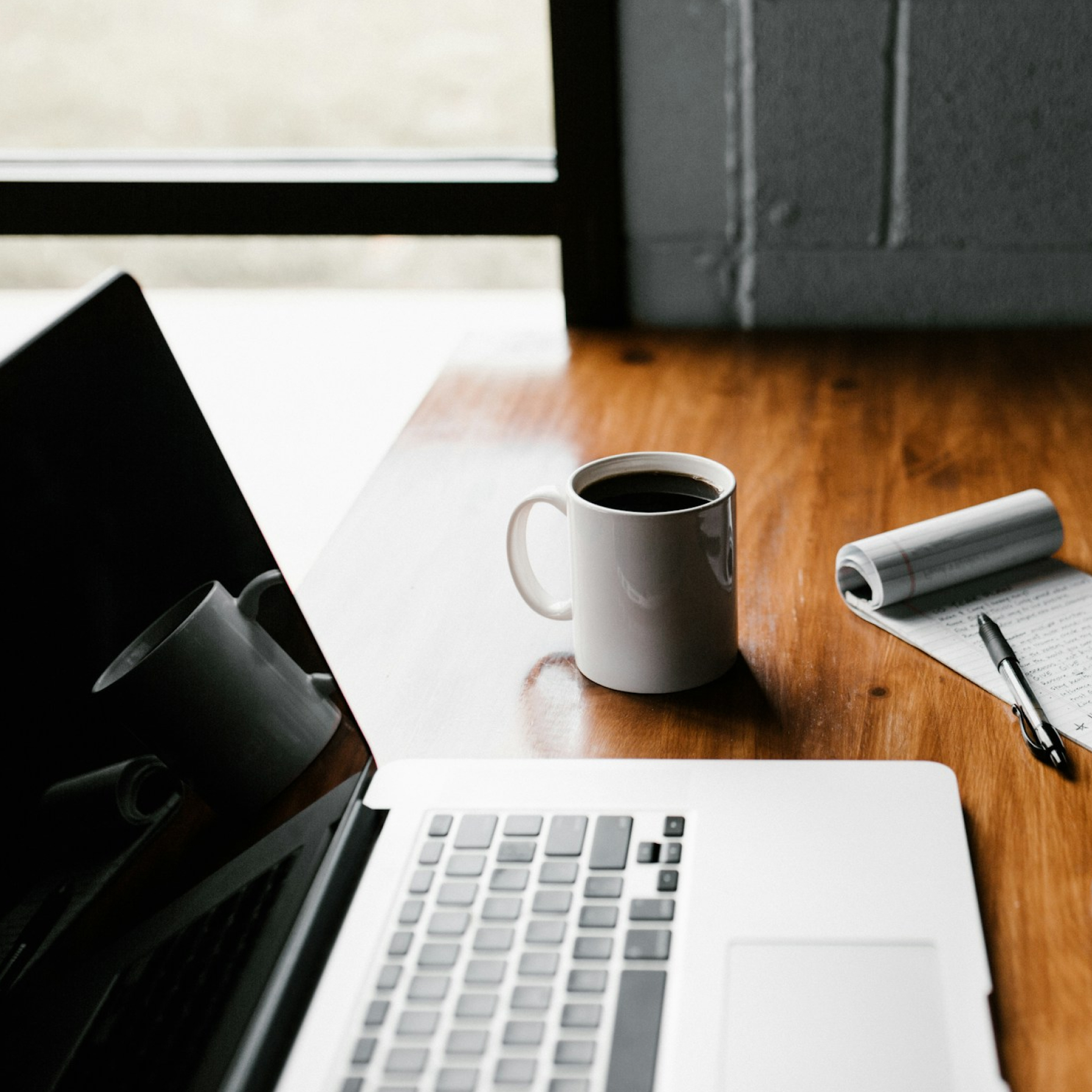 A coffee cup next to a laptop and notebook on a desk, representing automated workflow processes.